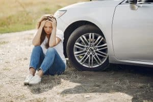 Woman sits on ground next to car reflecting on an automotive accident